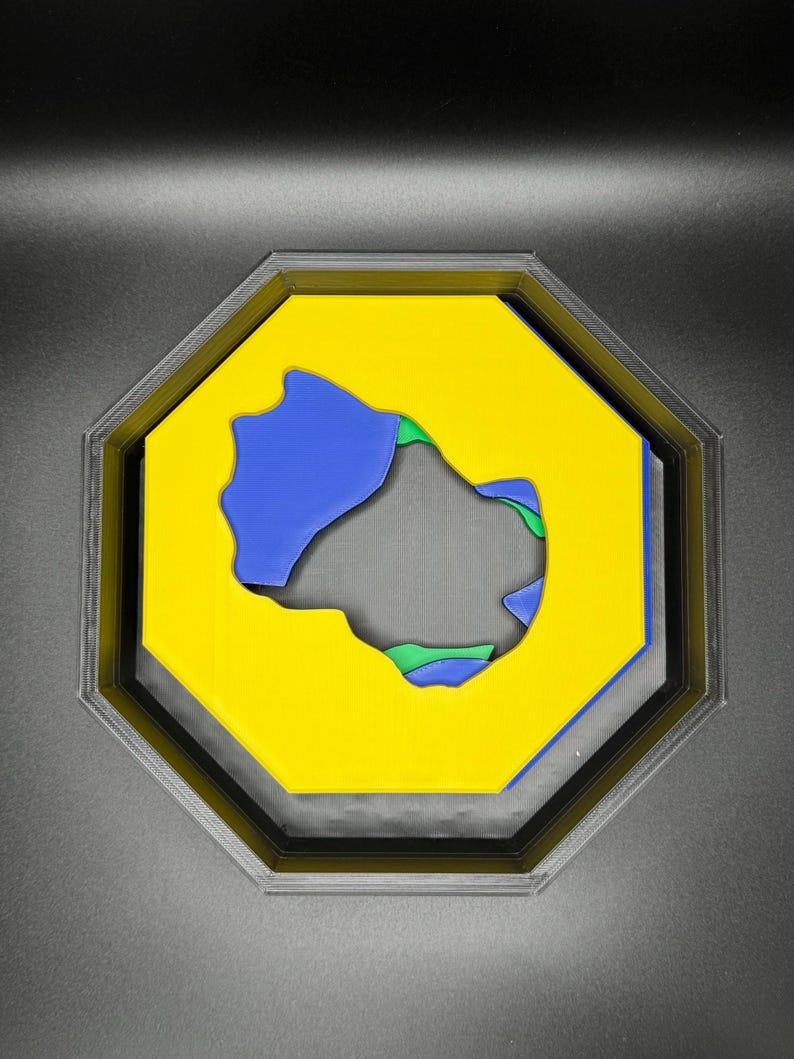 Op de afbeelding: Een geel achtkantig frame met een blauwe en groene uitsparing in het midden. Het frame is omgeven door een zwarte rand.
