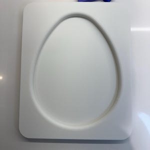 Op de afbeelding: Een witte keramische mal in de vorm van een ei met een verhoogde rand. De mal ligt op een wit oppervlak.