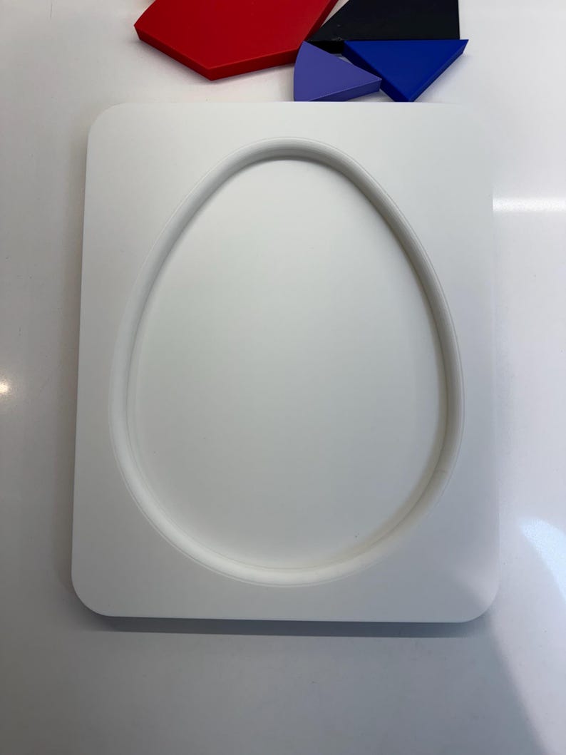 Op de afbeelding: Een witte keramische mal in de vorm van een ei met een verhoogde rand. De mal ligt op een wit oppervlak.