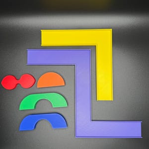May include: A set of colourful plastic shapes, including two red circles, a half-circle in orange, two green half-circles, and a blue half-circle. There are also two L-shaped frames, one in yellow and one in purple.