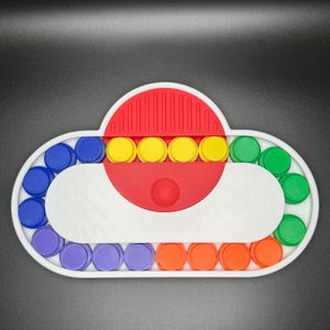 May include: A white cloud-shaped fidget toy with a red center and a row of yellow buttons. The cloud is surrounded by a ring of colorful buttons in purple, blue, green, and orange.