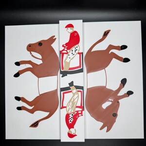 May include: A white paper craft with two brown paper donkeys and two red and white paper figures riding the donkeys. The figures are in a riding position, one is upright and the other is upside down.
