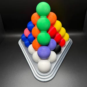 May include: A pyramid-shaped puzzle made of colorful balls. The balls are arranged in a triangular pattern, with the largest ball at the top and the smallest balls at the bottom. The puzzle is made of plastic and is designed to be challenging and fun.