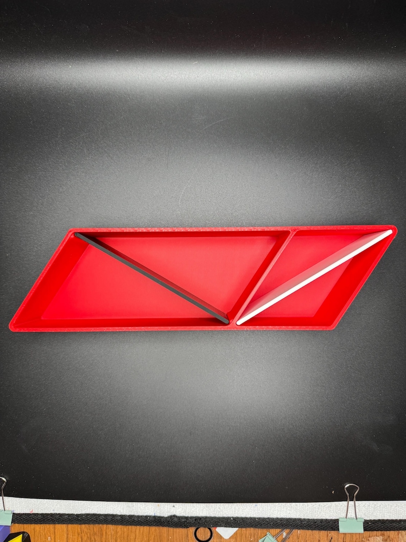 May include: A red, triangular-shaped tray with three compartments. The compartments are divided by black and white dividers. The tray is made of plastic.