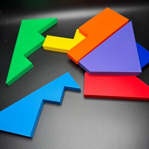 May include: A set of six colorful puzzle pieces made of wood. The pieces are shaped like different geometric shapes, including triangles, squares, and rectangles. The pieces are arranged in a random order on a black surface.