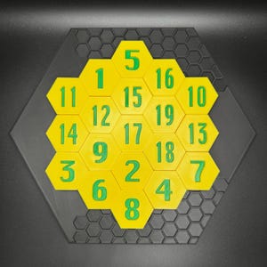 Puede incluir: Un rompecabezas hexagonal amarillo con n&uacute;meros verdes del 1 al 19. El rompecabezas est&aacute; sobre un fondo negro.