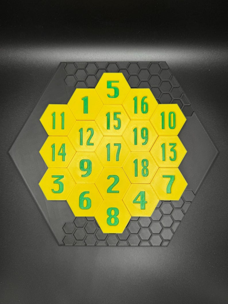 Puede incluir: Un rompecabezas hexagonal amarillo con n&uacute;meros verdes del 1 al 19. El rompecabezas est&aacute; sobre un fondo negro.
