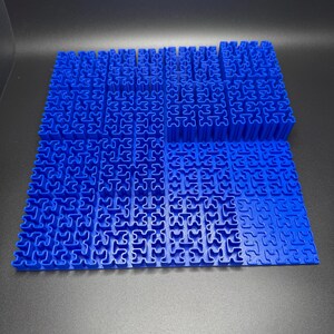 May include: A blue plastic puzzle with interlocking pieces. The puzzle is made up of many small squares, each with a unique shape. The puzzle is arranged in a grid pattern.