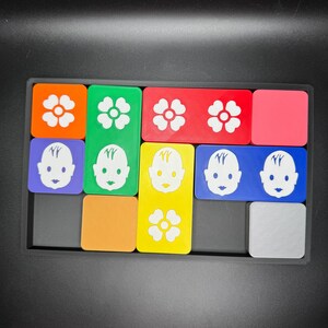 May include: A colorful puzzle with different shaped pieces. Each piece has a different image on it, including flowers and faces. The puzzle is made of plastic and is in a black frame.