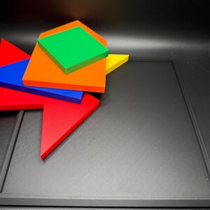 May include: A set of five colourful geometric shapes, including a red triangle, a blue triangle, an orange square, a green diamond, and a yellow triangle, arranged on a black surface.