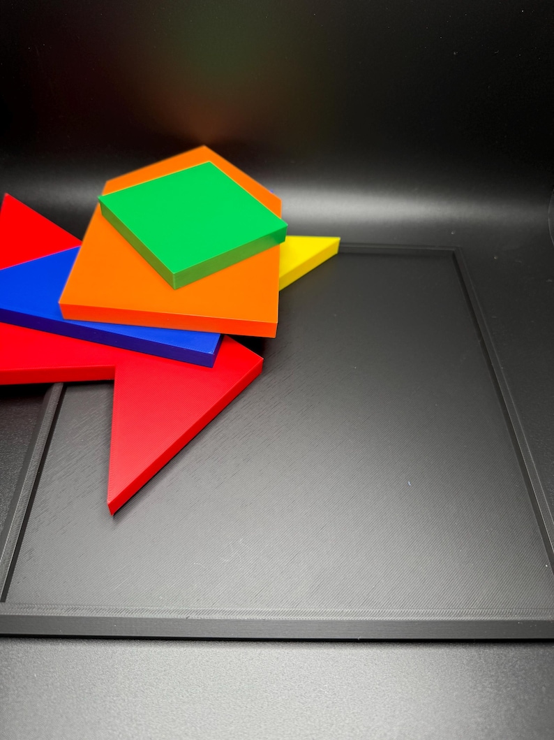 May include: A set of five colourful geometric shapes, including a red triangle, a blue triangle, an orange square, a green diamond, and a yellow triangle, arranged on a black surface.