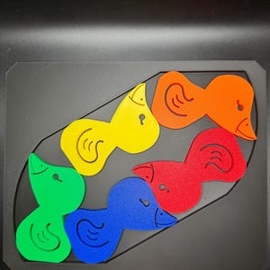 May include: A colorful wooden puzzle featuring six duck-shaped pieces in green, blue, red, yellow, and orange. The puzzle pieces fit into a black rectangular base, designed for children's educational play.