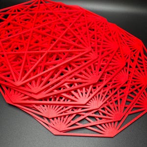 May include: A stack of red octagonal placemats with a geometric design. The placemats are made of a thin, flexible material and have a delicate, intricate pattern.