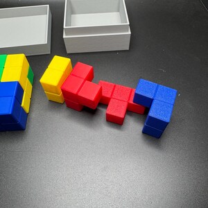 Puede incluir: Un conjunto de bloques de tipo Tetris de colores rojo, azul, amarillo y verde. Los bloques est&aacute;n dispuestos en un patr&oacute;n y est&aacute;n sobre una superficie gris.