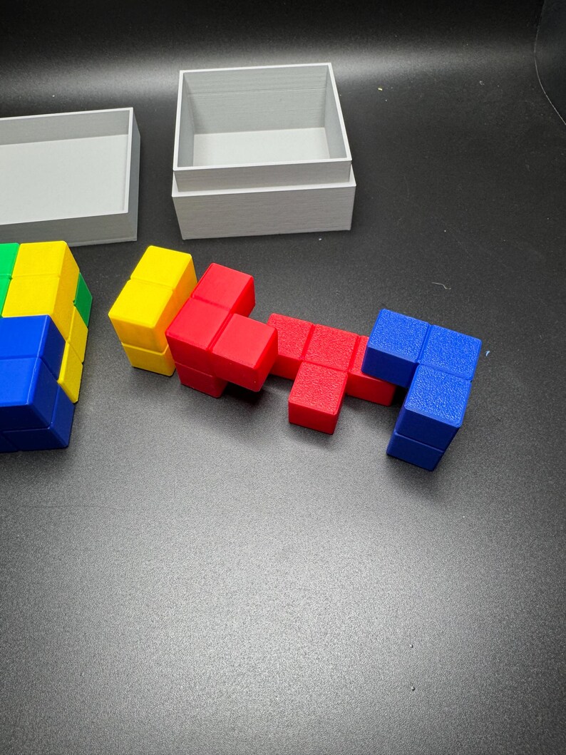 Puede incluir: Un conjunto de bloques de tipo Tetris de colores rojo, azul, amarillo y verde. Los bloques est&aacute;n dispuestos en un patr&oacute;n y est&aacute;n sobre una superficie gris.