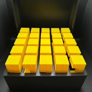 May include: A black box with a lid open, revealing a grid of 25 bright yellow cubes.