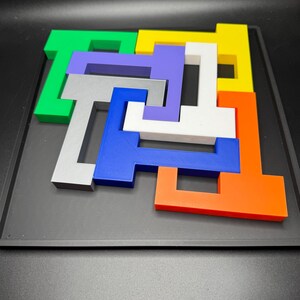 Op de afbeelding: Een kleurrijke puzzel met zeven stukken in verschillende vormen en kleuren. De stukken zijn in een patroon op een zwarte achtergrond gerangschikt.