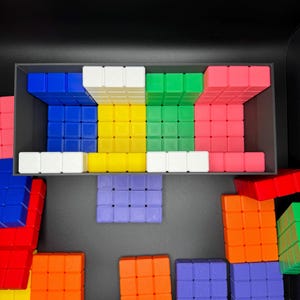 May include: A set of colorful plastic blocks in various shapes and sizes. The blocks are arranged in a pattern on a black surface. The blocks are red, blue, green, yellow, white, and orange.