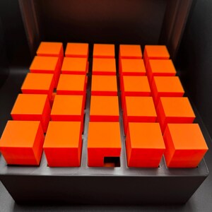 May include: A black box with a grid of 36 orange cubes. One cube is missing from the center of the grid.
