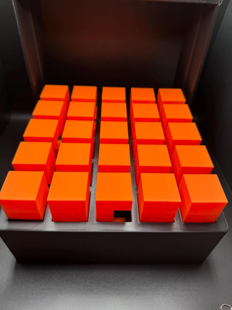 May include: A black box with a grid of 36 orange cubes. One cube is missing from the center of the grid.