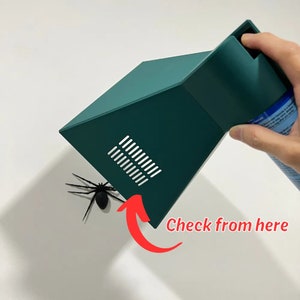 May include: A green plastic trap with a small opening and a black spider model inside. The trap is designed to catch spiders and other insects. The text "Check from here" is written on the image.