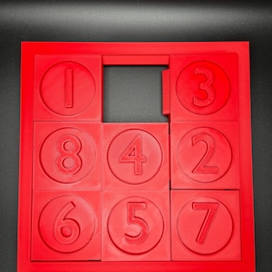 May include: A red sliding puzzle with nine numbered tiles. The tiles are arranged in a 3x3 grid with one tile missing. The numbers on the tiles are 1, 2, 3, 4, 5, 6, 7, 8, and a blank space.