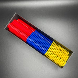May include: A black rectangular box filled with colorful plastic pieces. The pieces are stacked in three sections: red, blue, and yellow.
