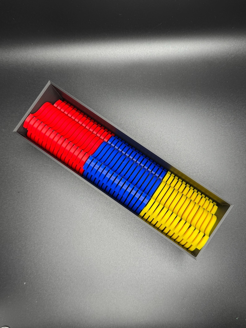 May include: A black rectangular box filled with colorful plastic pieces. The pieces are stacked in three sections: red, blue, and yellow.