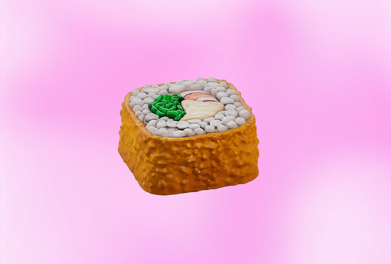 May include: A single piece of sushi with a crispy, golden brown exterior. The sushi is filled with white rice, a green vegetable, and a pink fish.