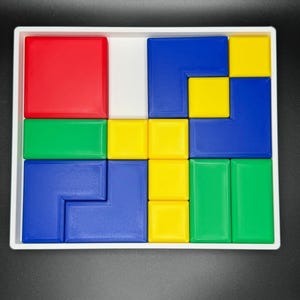 May include: A white tray with a puzzle made of colorful plastic blocks. The blocks are red, green, blue, and yellow. The puzzle is in a solved state.