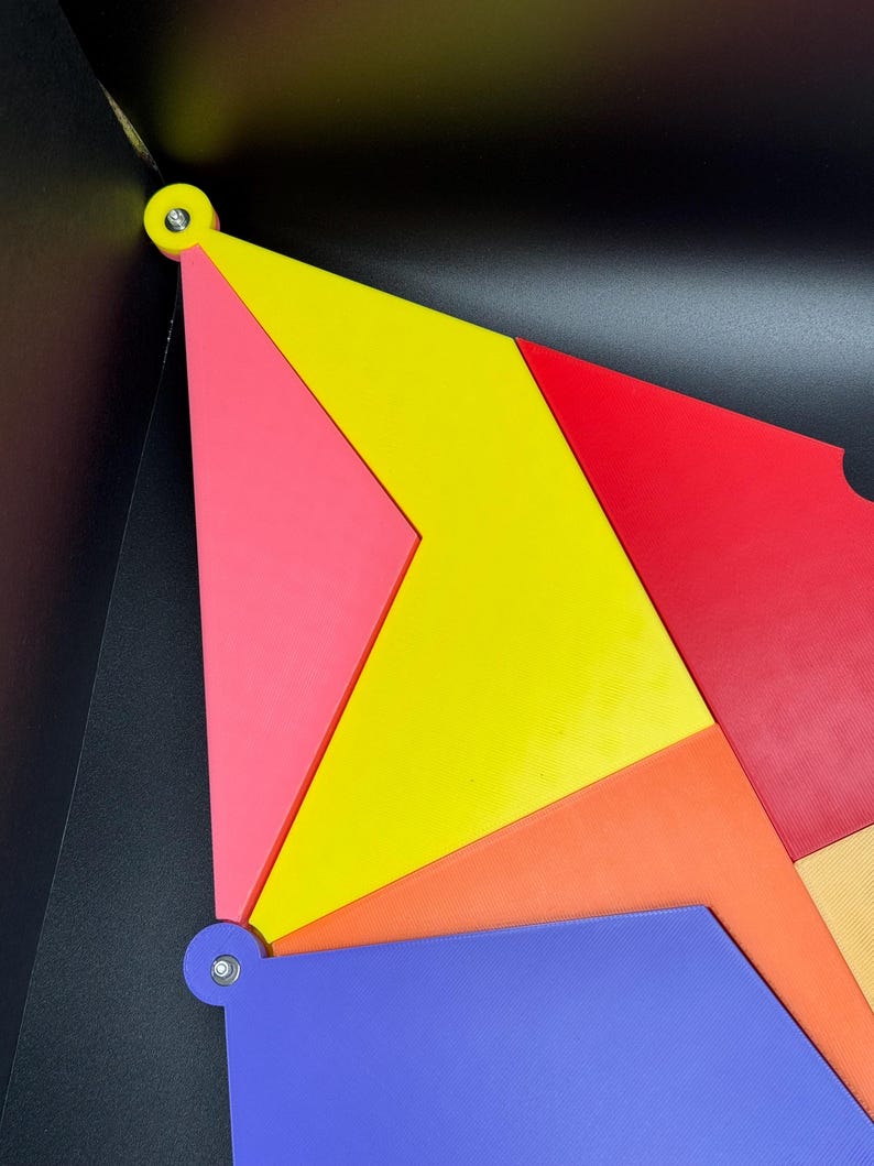 Peut inclure: Composition g&eacute;om&eacute;trique abstraite avec des formes vives et imbriqu&eacute;es en rouge, jaune, rose, orange et bleu. Les pi&egrave;ces sont fix&eacute;es avec de petites attaches argent&eacute;es sur un fond noir. Le design est moderne et color&eacute;.