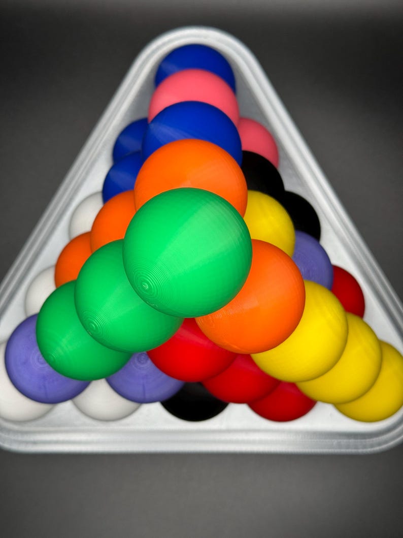 May include: A triangle-shaped rack holds a set of colorful billiard balls, including red, green, blue, yellow, orange, black, and white.