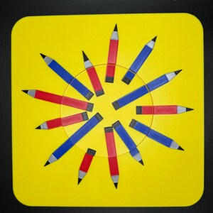 Op de afbeelding: Een geel vierkant met een cirkel van rode en blauwe potloden die in een radiaal patroon zijn gerangschikt. De potloden wijzen allemaal naar buiten vanaf het midden van de cirkel.