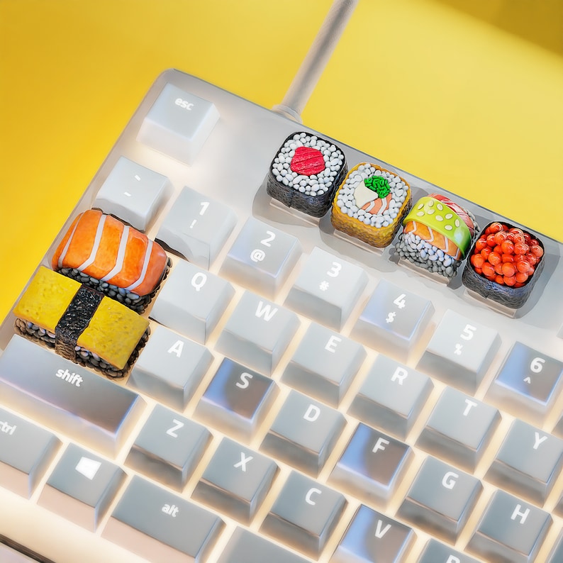 May include: A white computer keyboard with keys labeled with letters and numbers.  The keys are decorated with small, colorful sushi pieces.