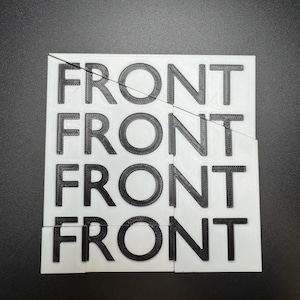 May include: A white, rectangular puzzle with the word "FRONT" printed in black, repeated four times. The puzzle is broken into several pieces, with the text visible on each piece. The background is a solid black surface.