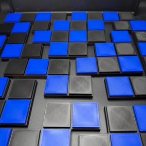 May include: A checkerboard pattern of alternating black and blue squares. The squares are raised and arranged in a grid, creating a 3D effect. The color scheme is a striking contrast of black and bright blue.