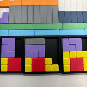 May include: A close-up of a puzzle game with three sections. Each section has a black frame and a different colored puzzle inside. The puzzles are made of small plastic squares in various colors, including red, yellow, purple, and gray.
