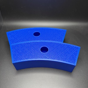 May include: Two bright blue, curved, 3D-printed objects. Each has a textured surface and a circular hole in the center. The objects are likely designed to hold or support something, possibly a cup or a small item.