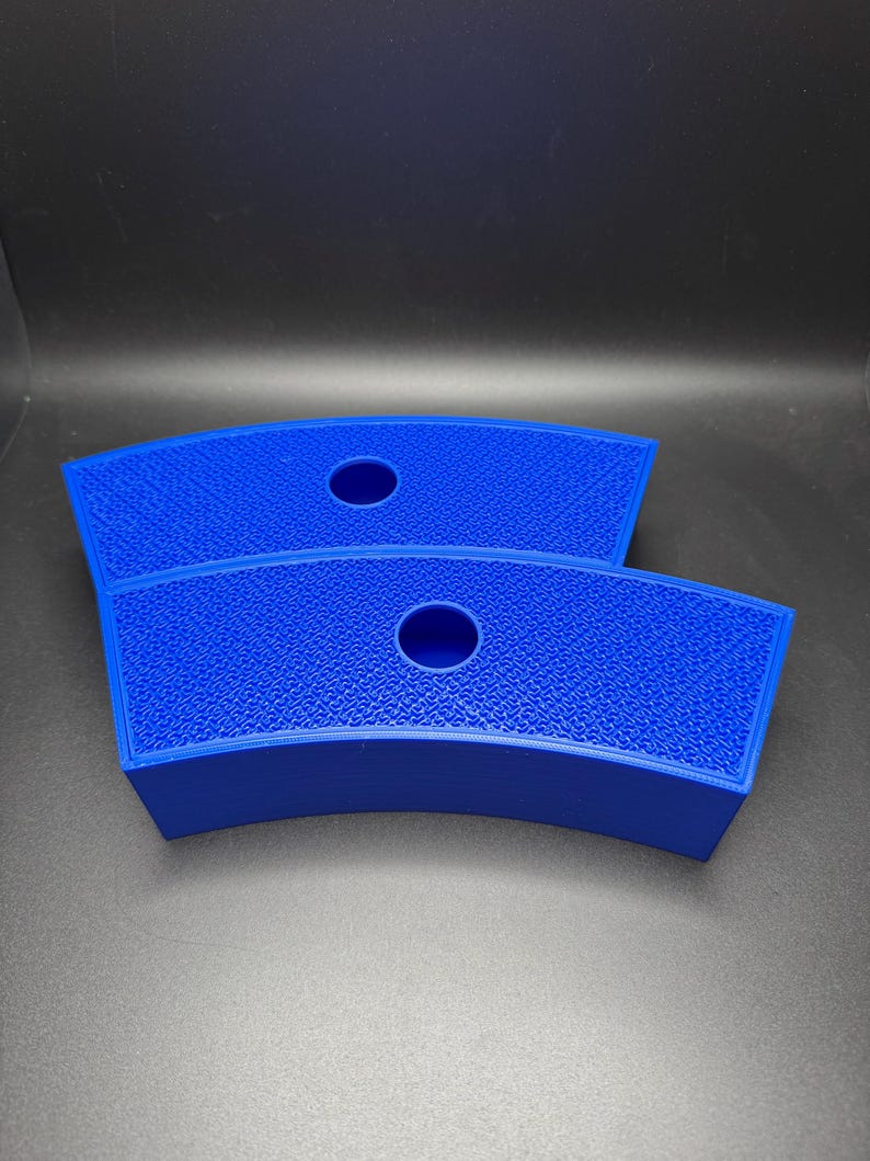 May include: Two bright blue, curved, 3D-printed objects. Each has a textured surface and a circular hole in the center. The objects are likely designed to hold or support something, possibly a cup or a small item.