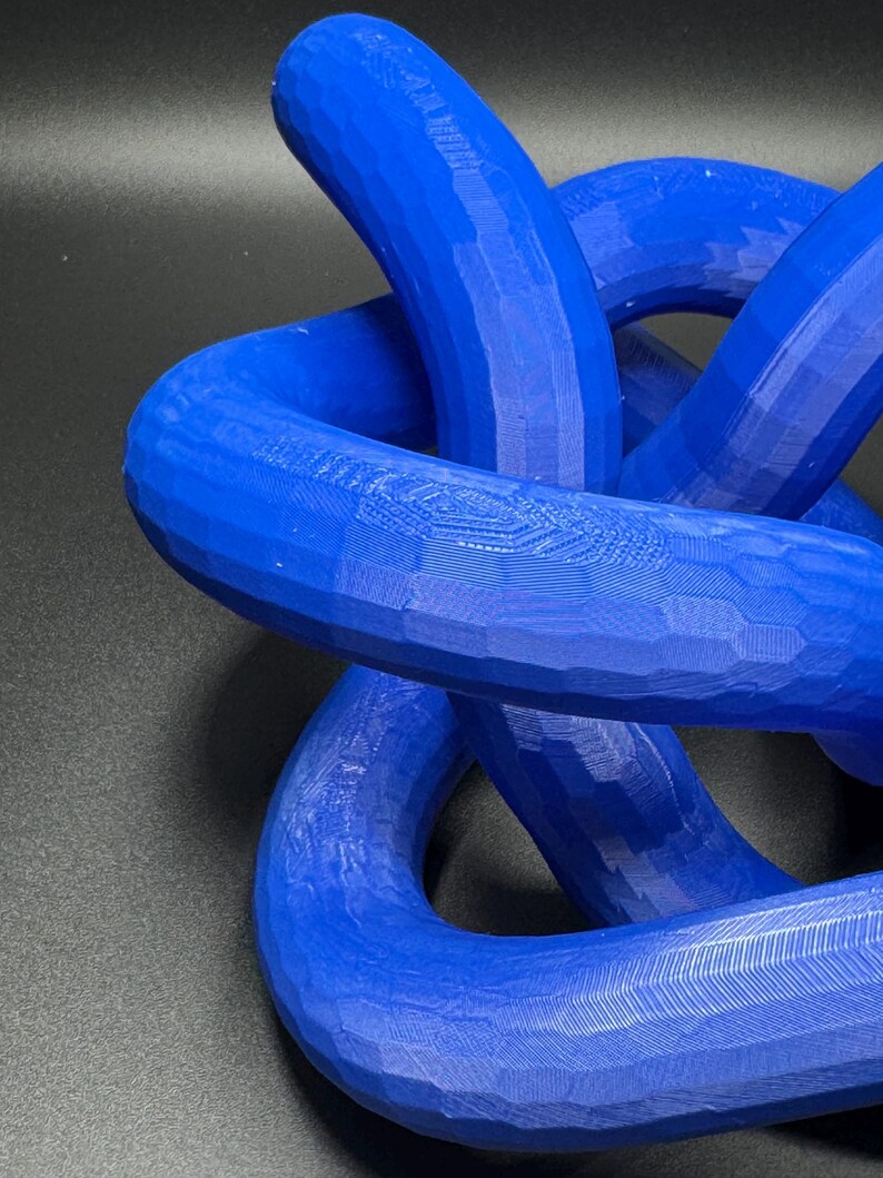 May include: A blue 3D printed knot sculpture. The knot is made of multiple intertwined loops, creating a complex and intricate design.