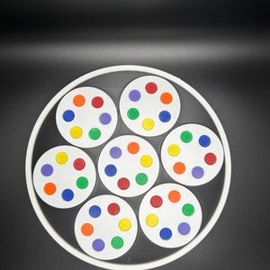 May include: A white circular tray with seven smaller white circles, each with six colorful dots. The dots are red, orange, yellow, green, blue, and purple. The tray has a black background.