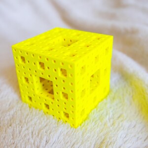May include: A yellow 3D printed cube with a geometric pattern of holes and squares.