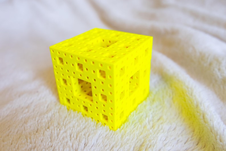 May include: A yellow 3D printed cube with a geometric pattern of holes and squares.