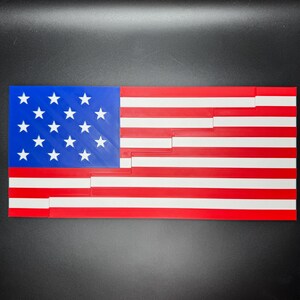 Puede incluir: Una bandera estadounidense impresa en 3D hecha de pl&aacute;stico rojo, blanco y azul. La bandera est&aacute; compuesta por piezas individuales que encajan para formar la bandera completa.