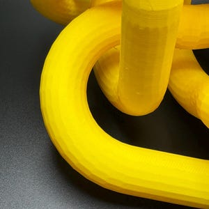 May include: A yellow 3D printed object with a complex, interwoven design. The object is made of plastic and has a smooth, glossy finish.