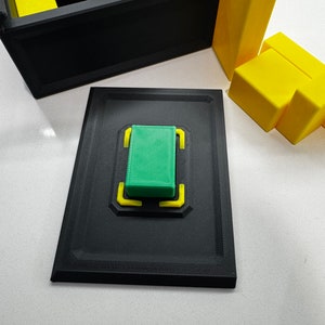 Pu&ograve; includere: Una scatola nera con un blocco verde all'interno. La scatola &egrave; aperta e il blocco verde &egrave; appoggiato su una piattaforma nera con accenti gialli. Ci sono blocchi gialli fuori dalla scatola.