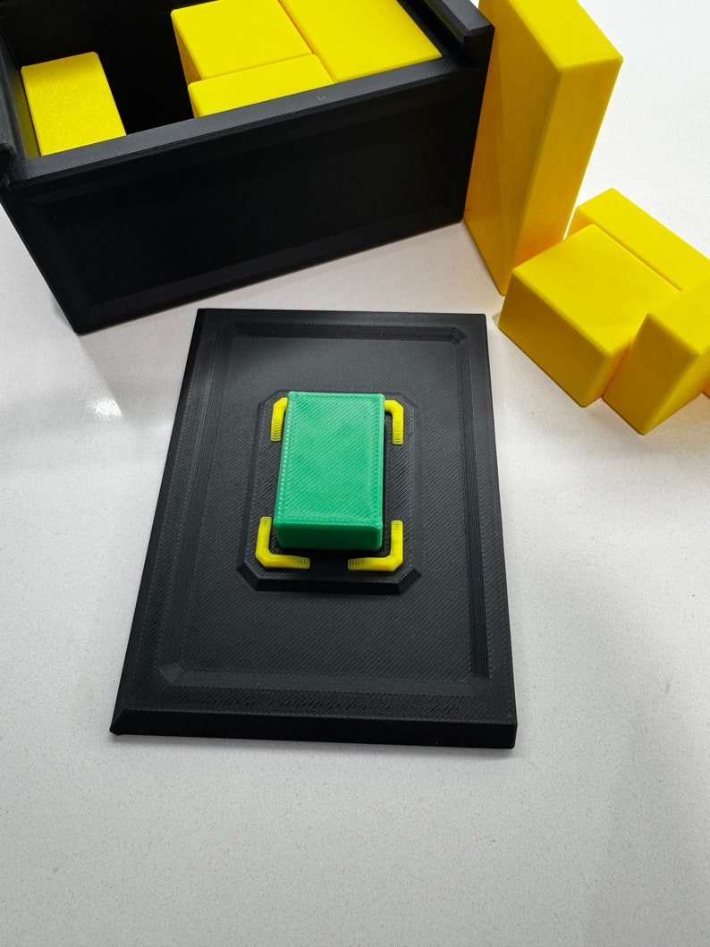 Pu&ograve; includere: Una scatola nera con un blocco verde all'interno. La scatola &egrave; aperta e il blocco verde &egrave; appoggiato su una piattaforma nera con accenti gialli. Ci sono blocchi gialli fuori dalla scatola.