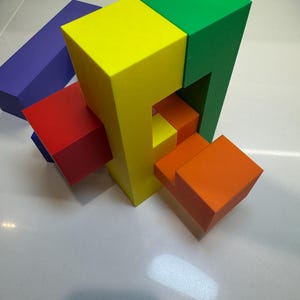 May include: A colorful wooden puzzle with five blocks in different colors: yellow, green, red, orange, and purple. The blocks are arranged in a complex pattern, creating a challenging puzzle.