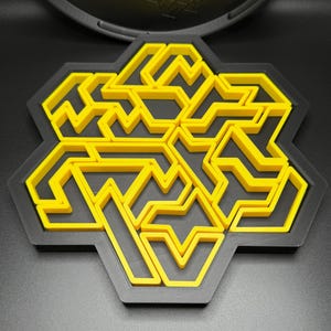 May include: A yellow and black geometric puzzle with a hexagonal shape. The puzzle is made of interlocking pieces that form a complex pattern.