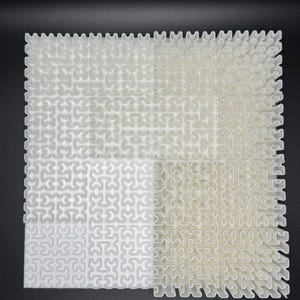 May include: A white plastic puzzle with a grid pattern. The puzzle is made up of small, interlocking pieces. The puzzle is divided into four sections, with each section having a different pattern.